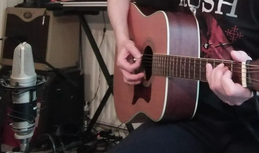 Photo of a microphone recording an acoustic guitar placed in front of the sound-hole but angled towards the 12th fret