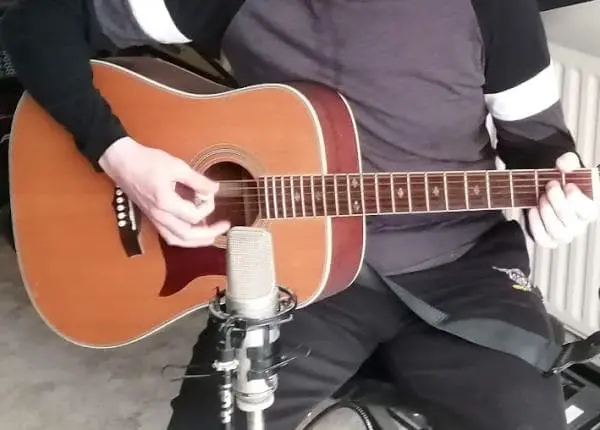 Photo of an acoustic guitar being recorded by a condenser microphone in a home studio
