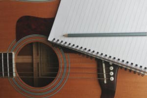 Photo of an acoustic guitar with a notebook and pencil resting on it