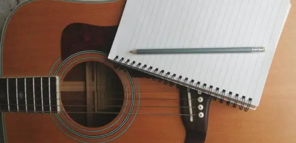 Photo of an acoustic guitar with a notebook and pencil resting on it