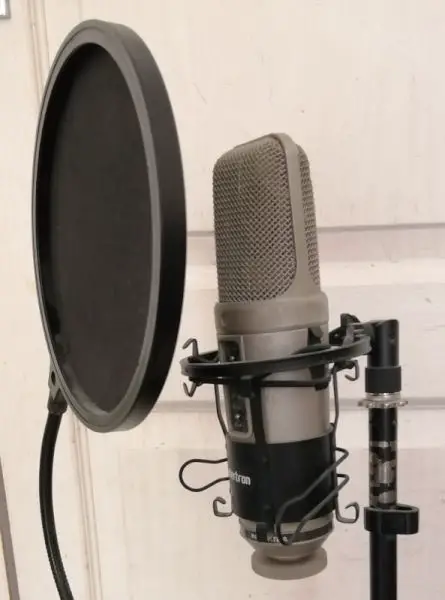Photo of an large diaphragm condenser microphone on a mic stand with a pop shield set up for vocal recording