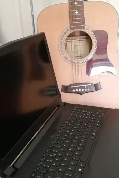 Photo of a laptop computer in the foreground with an acoustic guitar in the background