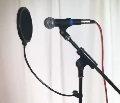 Photo of an SM58 dynamic microphone on a mic stand with a pop shield set up for vocal recording