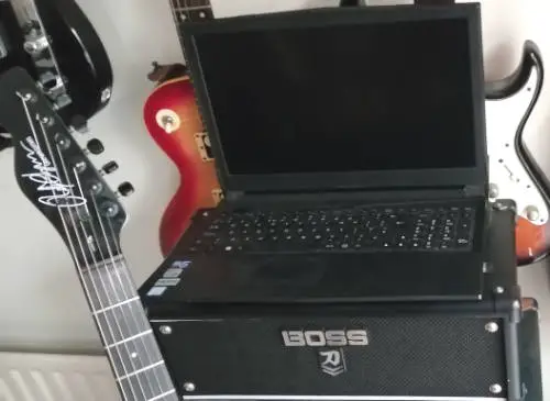 Photo of a laptop computer resting on a guitar amp, with some electric guitars