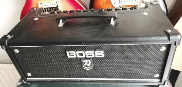 Photo of a Boss Katana Head guitar amp with two electric guitars in the background